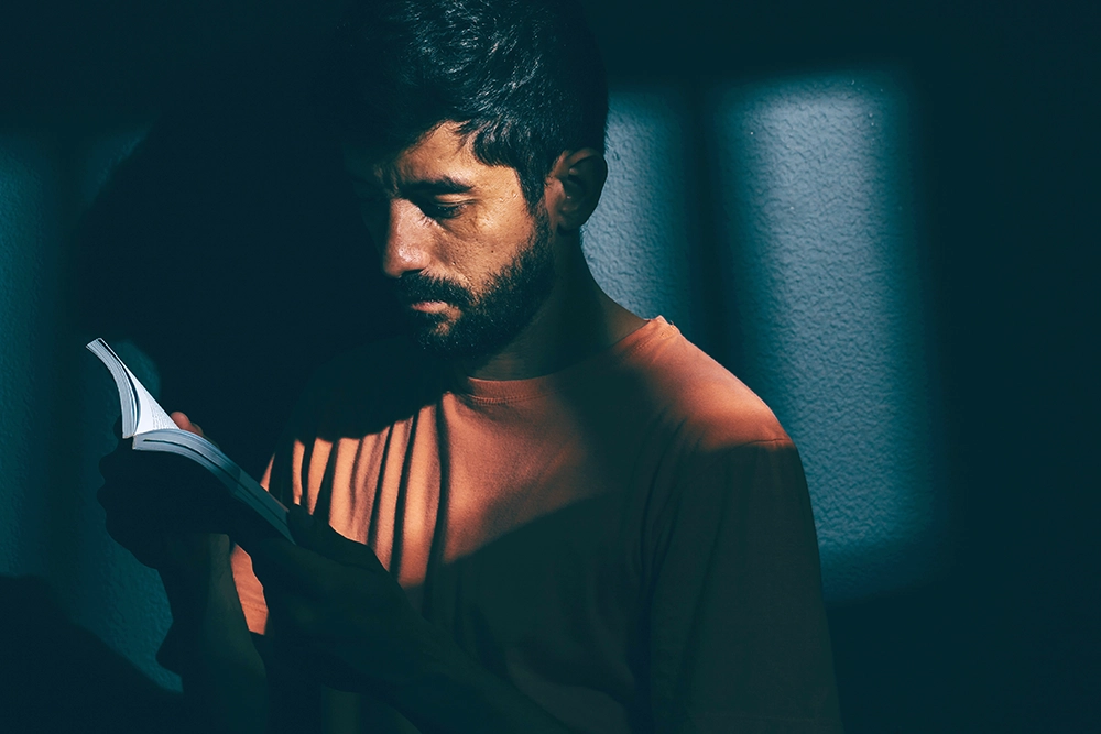 Man reading a Bible in dark prison cell